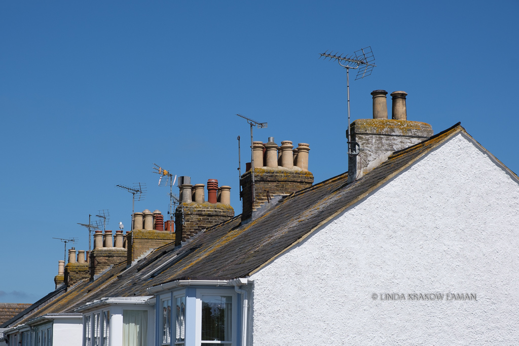 The rooves of the buildings, showing chimneys, chimney pots, and TV antennas against a blue cloudless sky. 