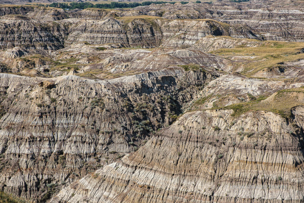 A closeup of the buttes. They have horizontal stripes of grey, brown, and black, and bits of grass on their flat tops. 