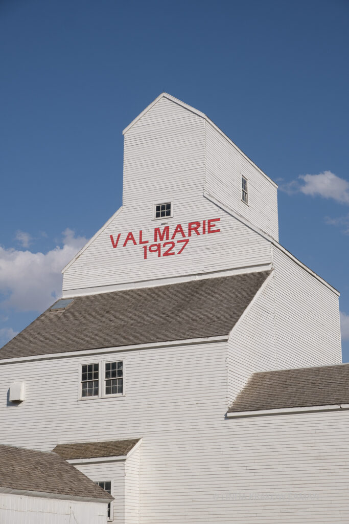 Closeup of a white wooden grain elevator reads "Val Marie 1927" in red   capital letters.