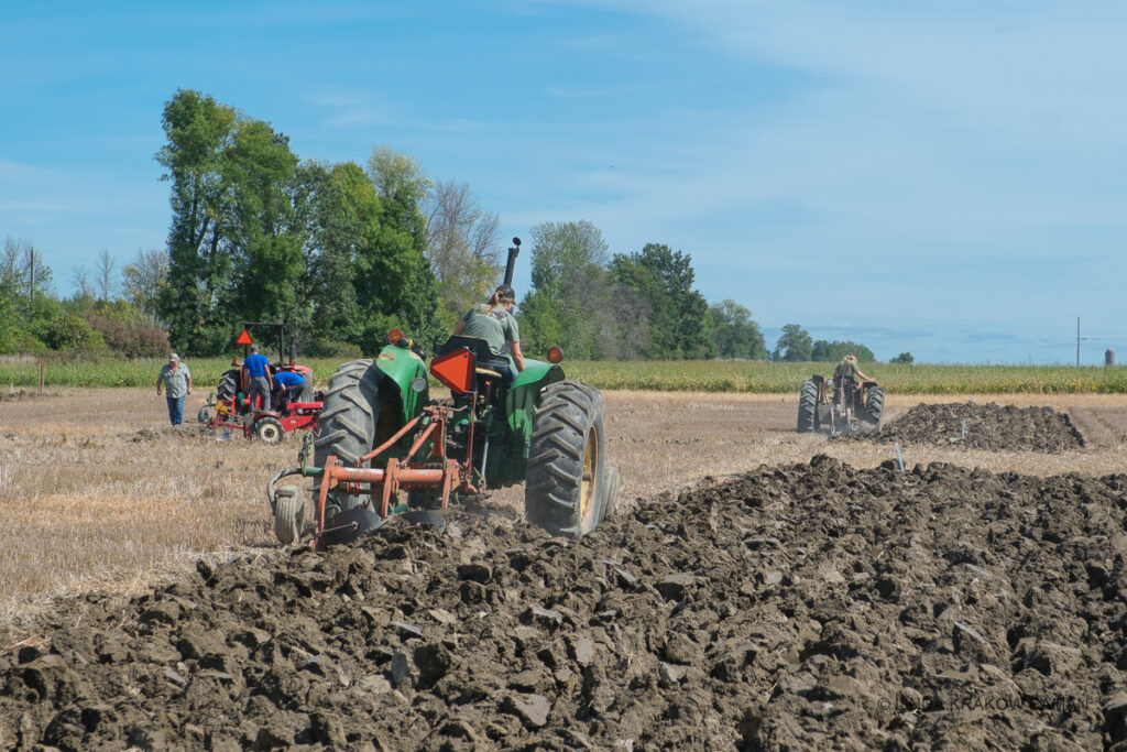 Three tractors are each plowing their own small section of a field
